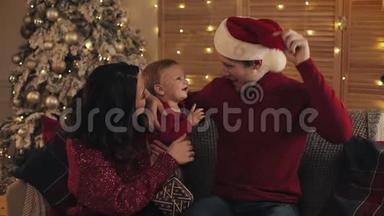 在舒适的家中度假背景下，爸爸妈妈和可爱的小男孩坐在沙发上靠近圣诞树